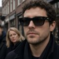 Man met een slimme camerabril in een Nederlandse winkelstraat, twee voorbijgangers kijken wantrouwend naar de bril