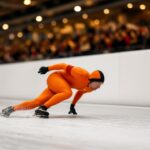 Mannelijke schaatser in oranje pak sprint over de lange baan van een overdekt ijsstadion, als beeld bij Nederlandse mannelijke schaatsers.