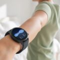 Smartwatch met slaapgrafiek aan de pols van iemand die zich uitrekt in een lichte slaapkamer