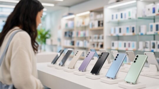Vrouw bekijkt een rij smartphones op een tafel in een lichte elektronicawinkel